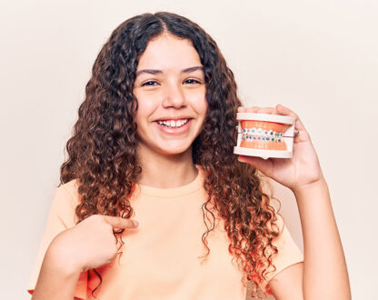Smiling girl holding a pair of teeth with braces explaining orthodontic treatment in Markham, ON are done.